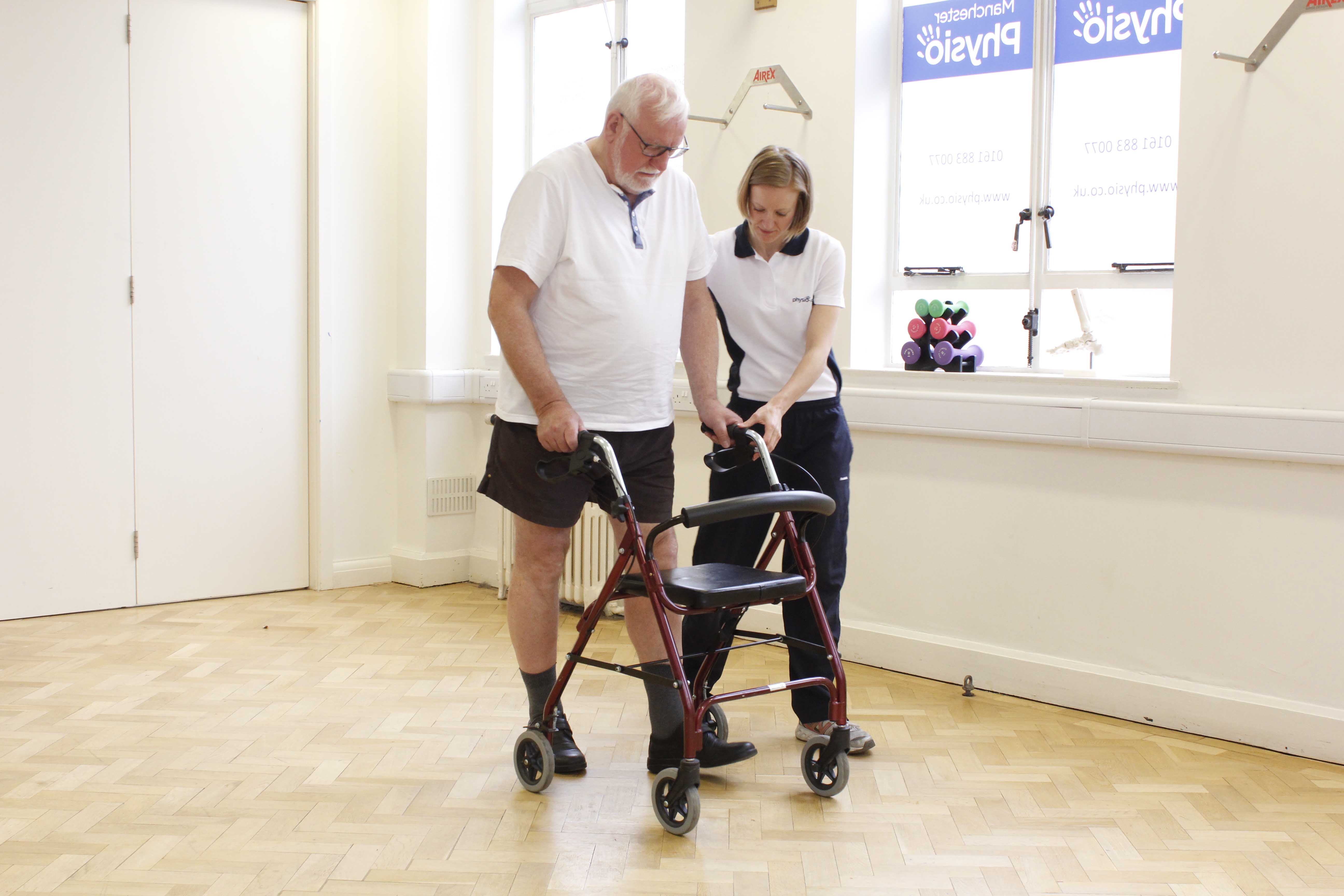 Specialist physiotherapist closely supervising mobility exercises using a rollator frame Specialist physiotherapist closely supervising mobility exercises using a rollator frame