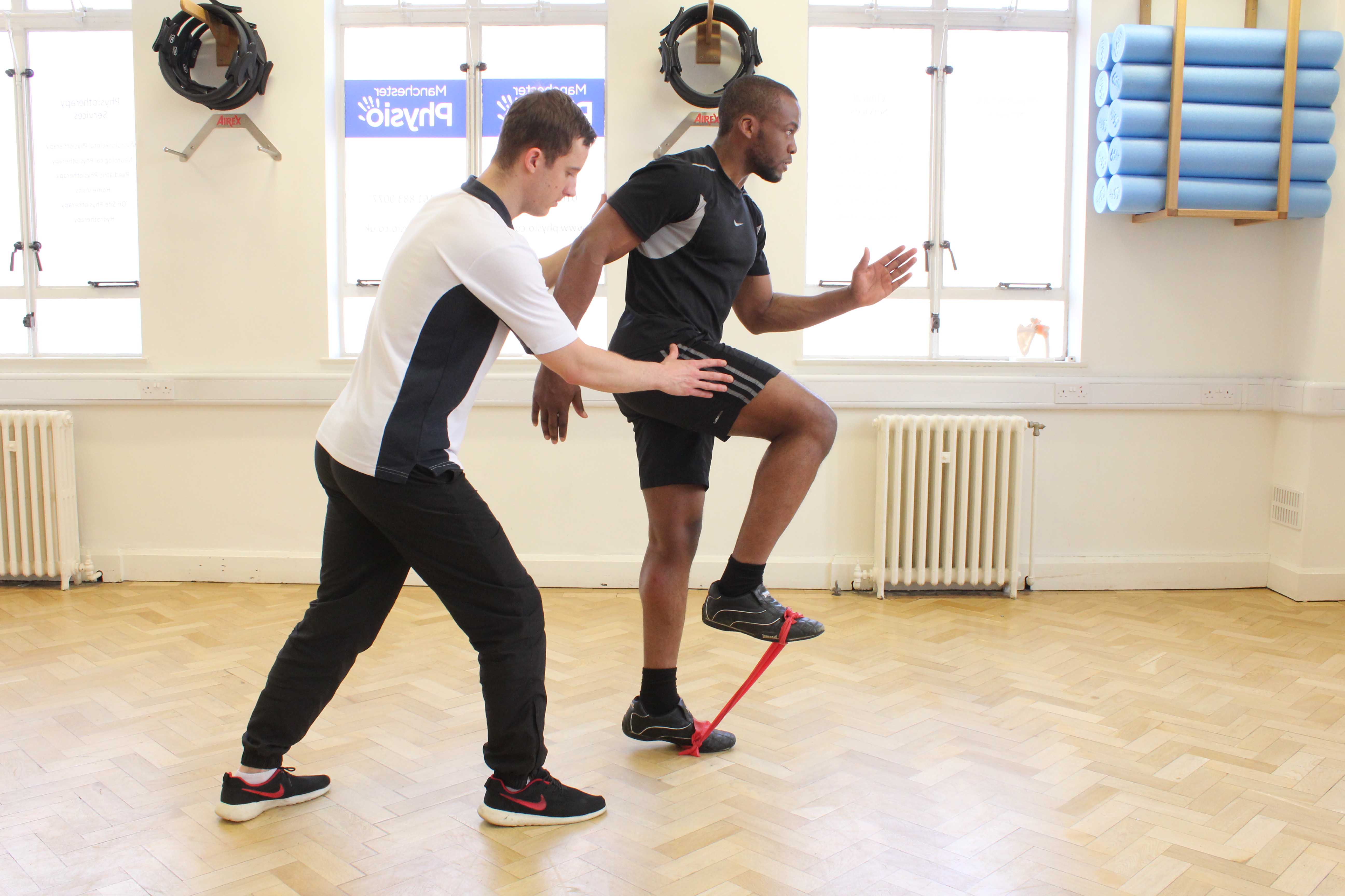 Physiotherapist supervising lower limb exercises using a resistance band.